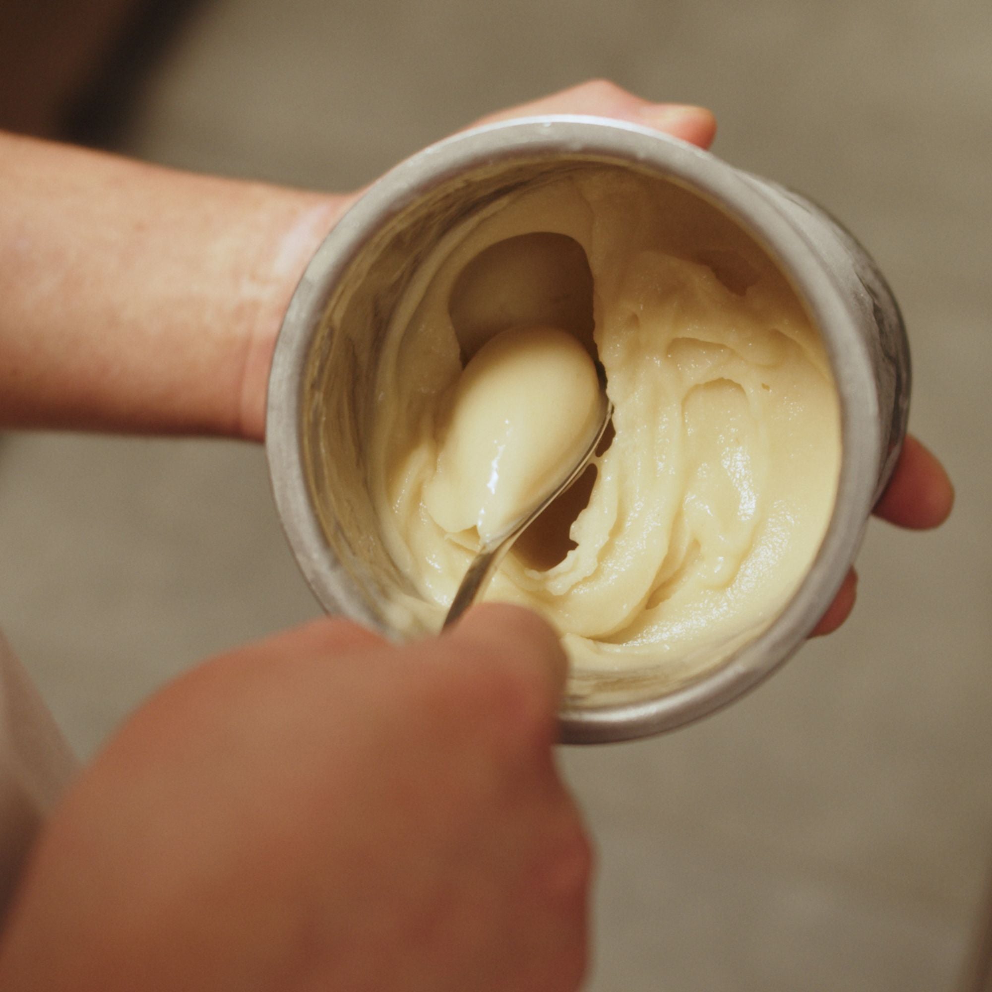 Hand scooping out ice cream from a container with a rocher spoon.