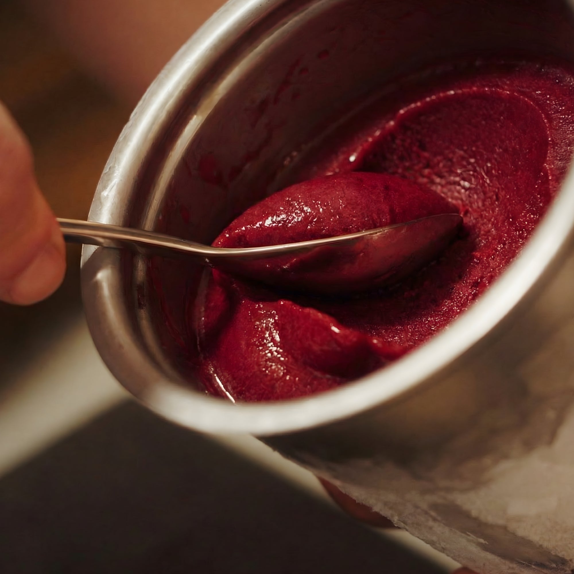 Berry ice cream being scooped from a pacojet with a small stainless steel rocher spoon.