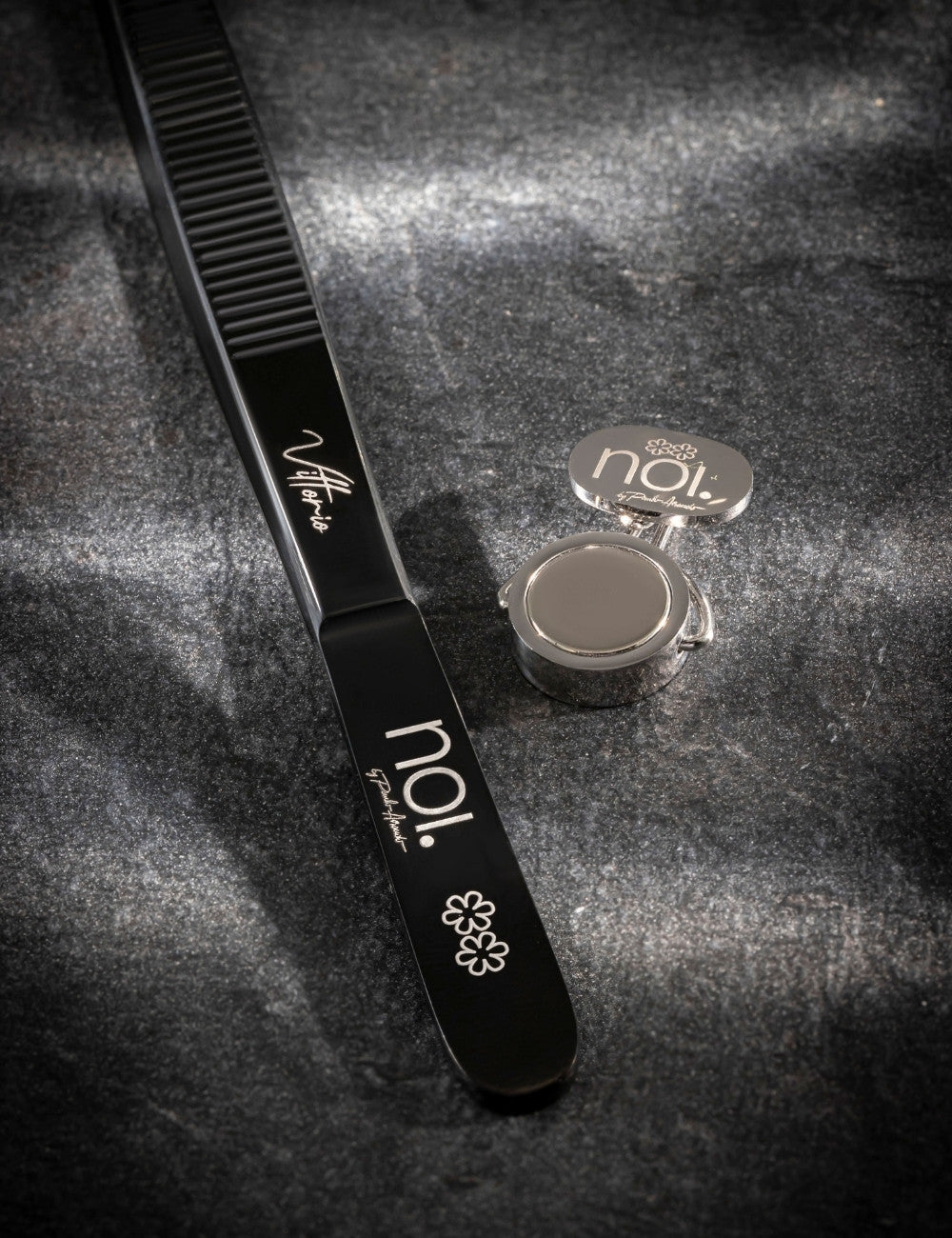 Black precision tweezers and the holdfast magnetic clip with "NOI by Paulo Airaudo" restaurant logo engraved on both.