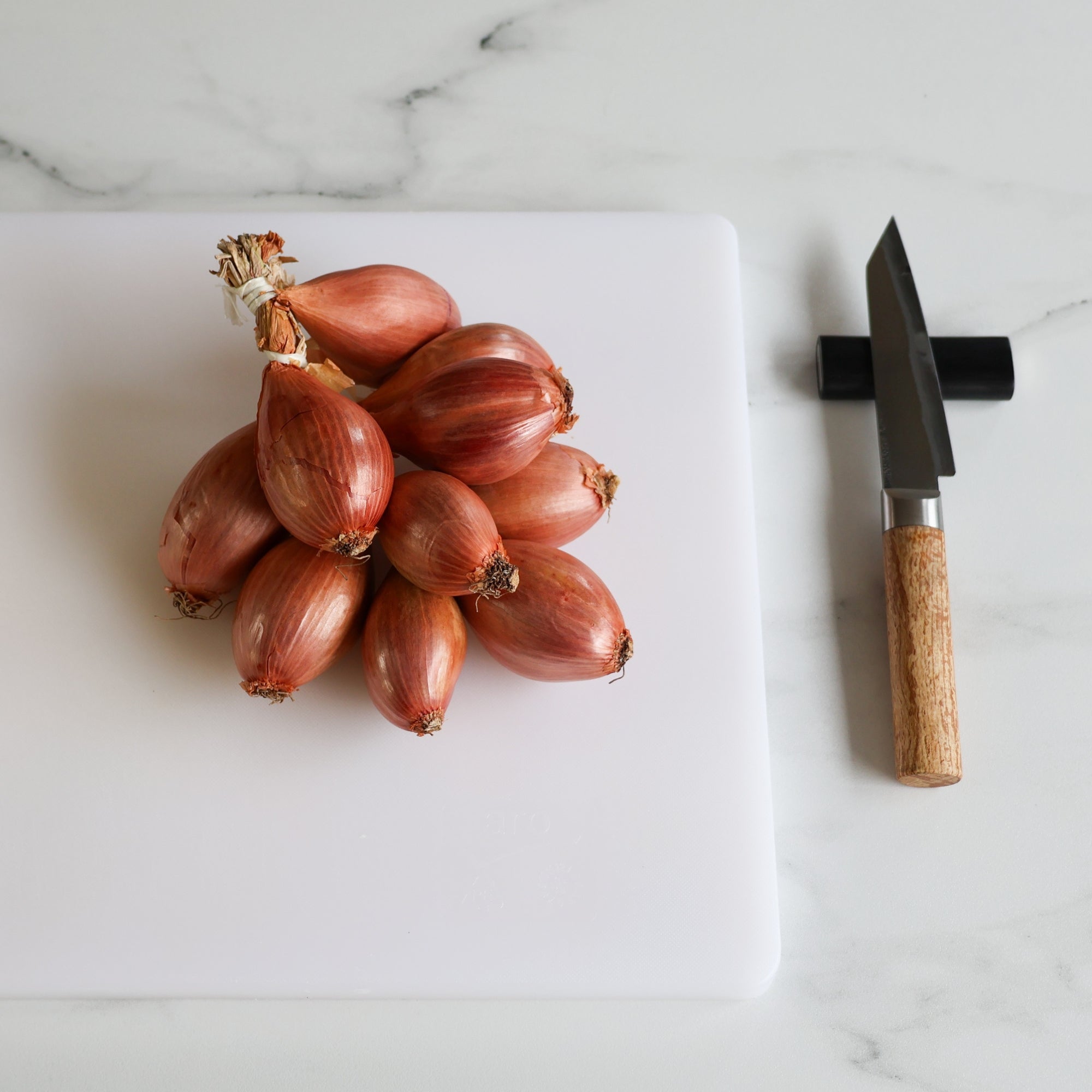 Modular laylow knife rest sitting on a kitchen marble countertop with a chefs knife resting on it, next to a chopping board.