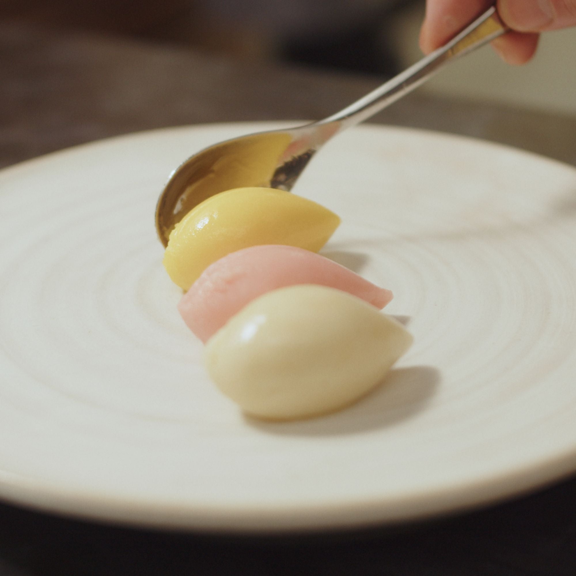 A Rocher of ice cream being dropped cleanly on to a white plate.
