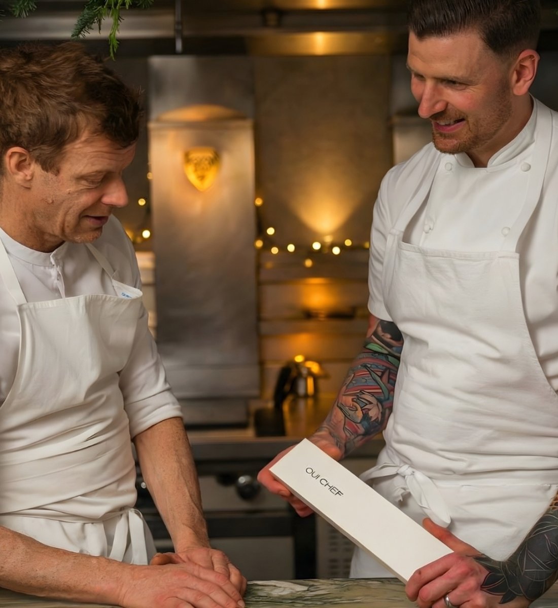 Two chefs in a kitchen setting, one holding a white tool kit box with 'Oui Chef' branding.